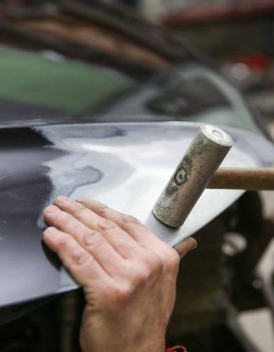 mechanic’s hands straighten the car body. mechanic is aligning car body part by hammer mechanic is aligning car body part by hammer